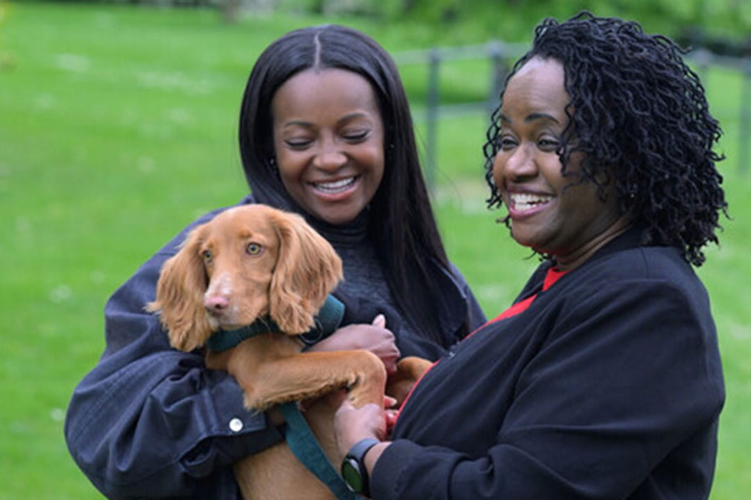 2 women smiling holding a dog