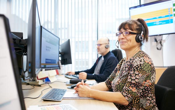 A female helpline worker, wearing headphones to take a call for Arthritis UK, supporting a person with arthritis.