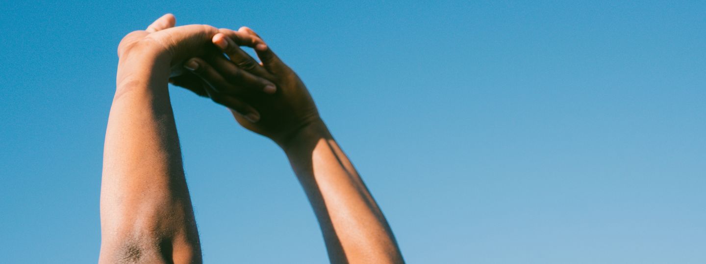 Hands stretching in front of blue sky