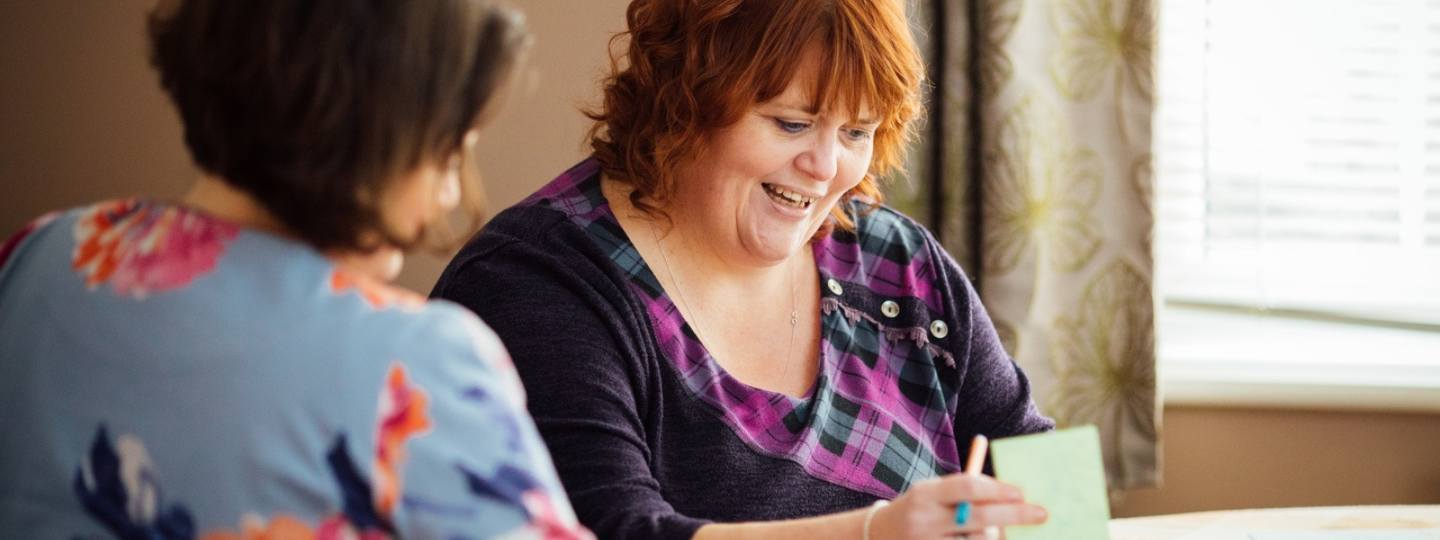 Deb, who has fibromyalgia, sitting beside another woman writing notes 
