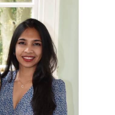 Smiling researcher Pratyasha wearing blue dress and red lipstick