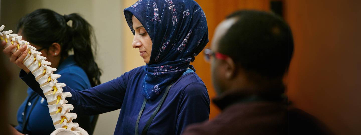 Woman wearing blue top and hijab holding a model of a spine