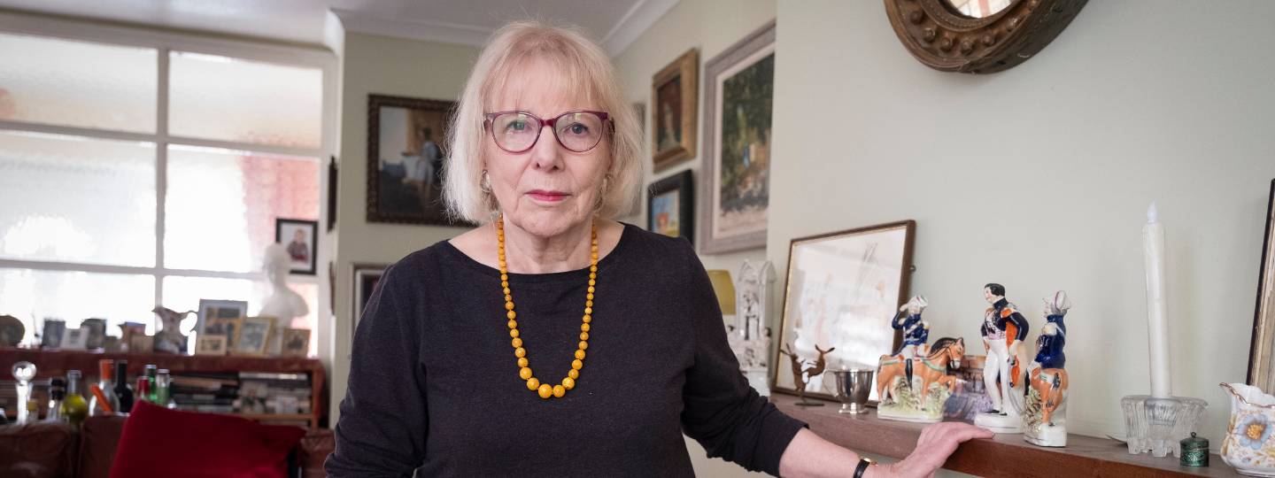 Roberta standing in her living room wearing yellow beaded necklace and black top