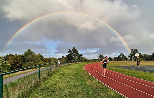 A man running on an athletics track with a rainbow behind him