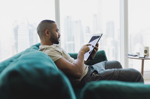 Researcher sitting on a couch using A Tablet to join an Arthritis UK PPIE Webinar